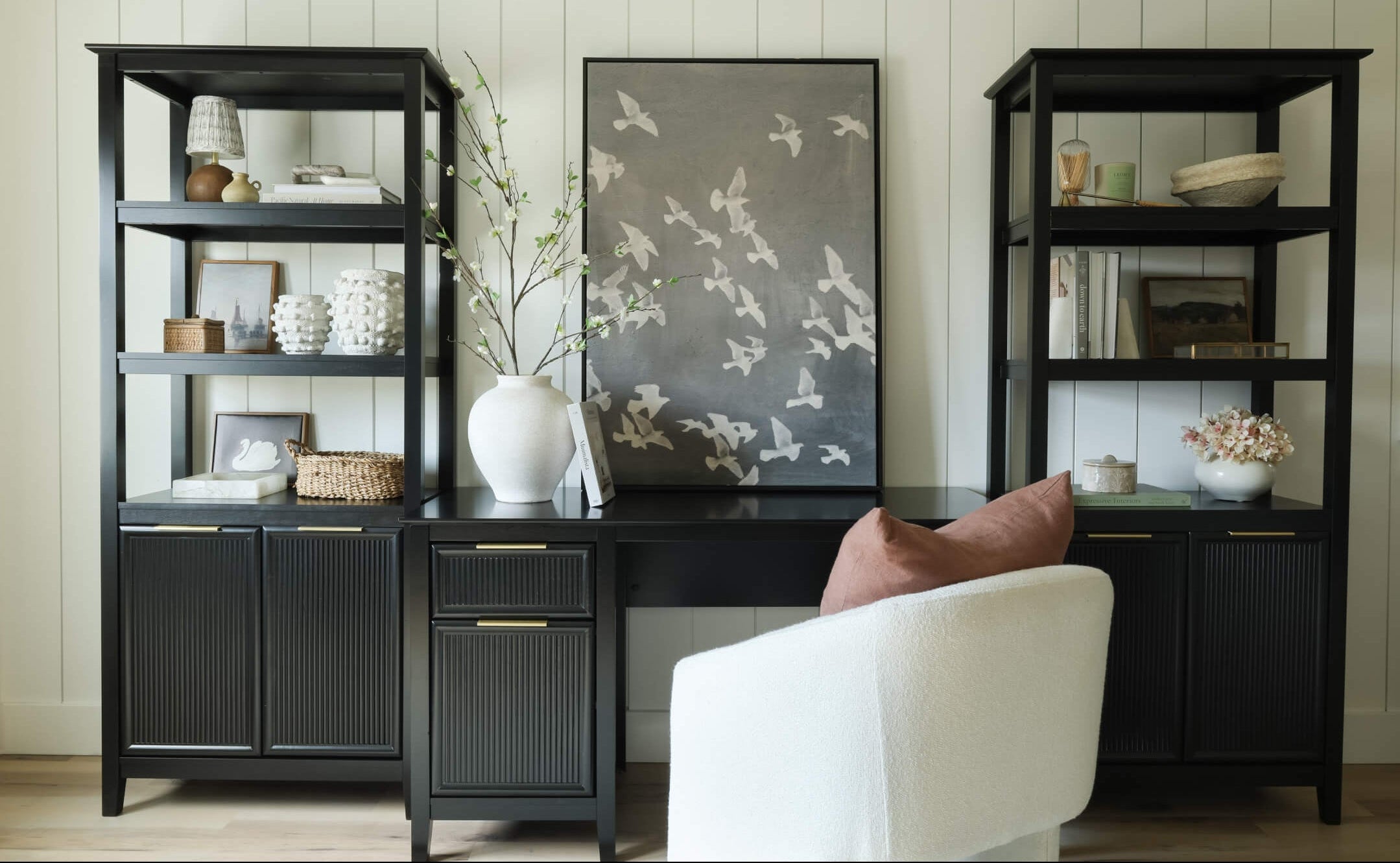 Black office desk with shelves and a chair in a room with white walls.