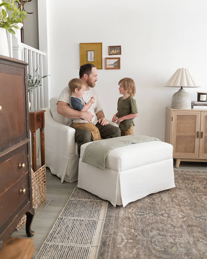 Man sitting on a white chair with two children in a home setting