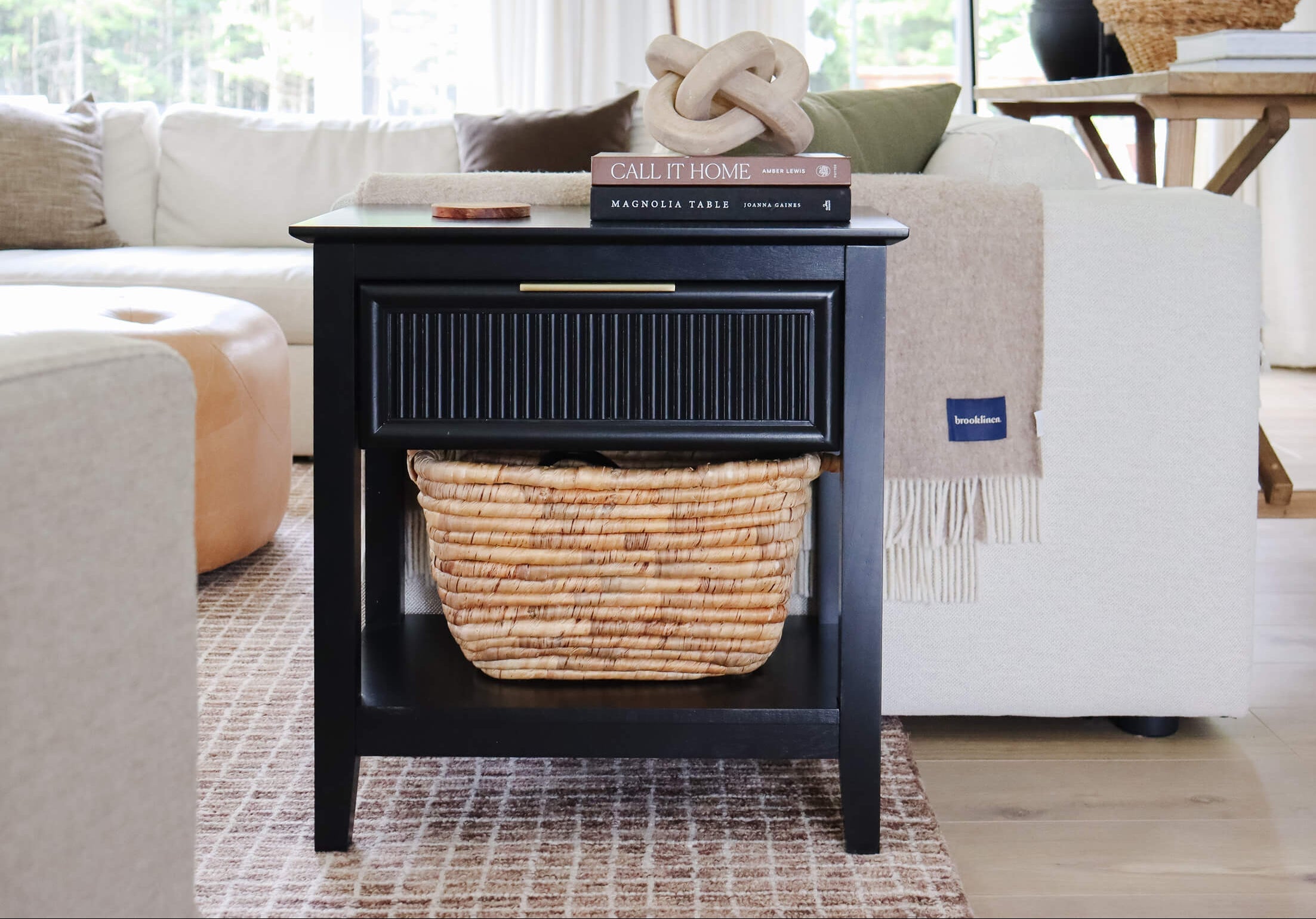 Black side table with a woven basket and books in a living room setting