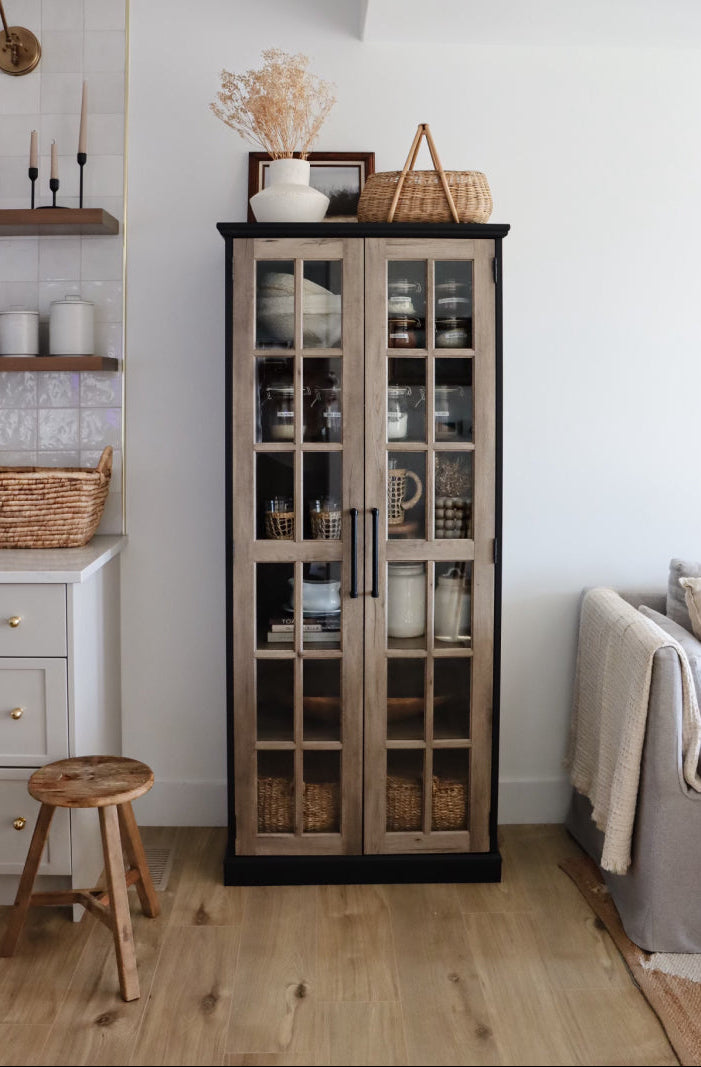 Tall glass-fronted cabinet in a living room setting with decor items on top